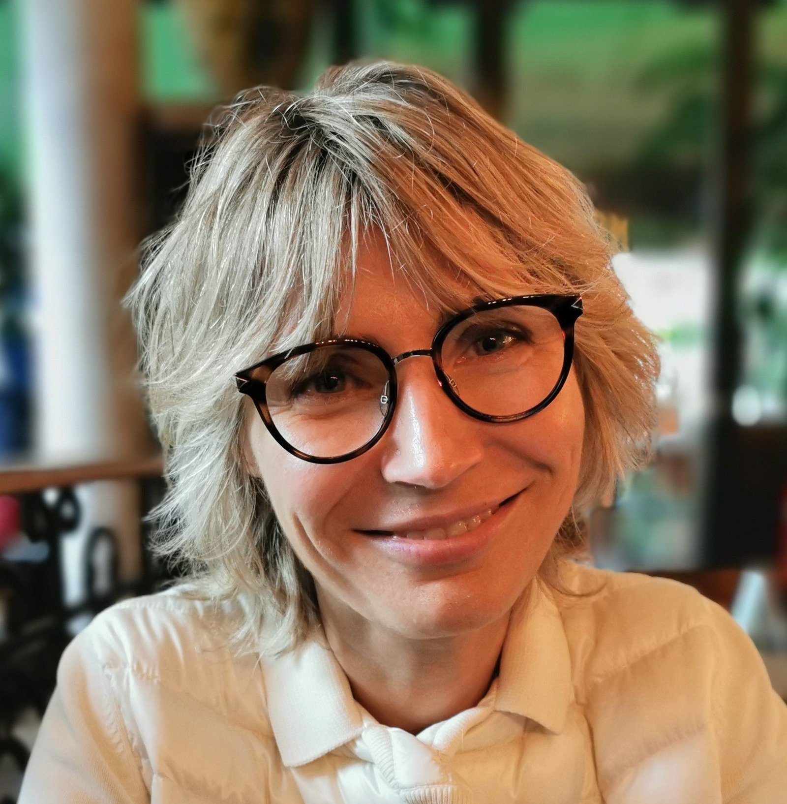Portrait of Anna, a smiling woman with blond hair and dark-rimmed glasses