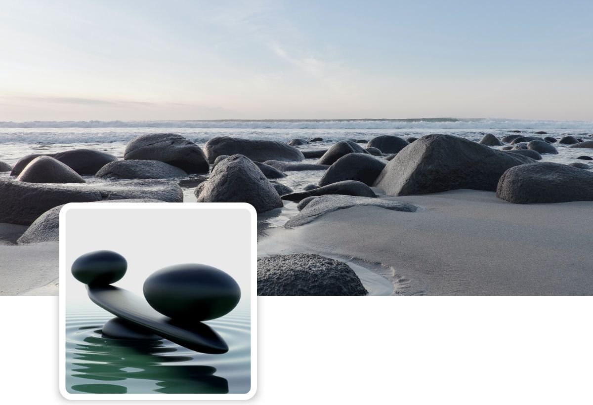Dark round stones on a calm sandy shore at dusk, with a small framed photo of balanced black stones on water