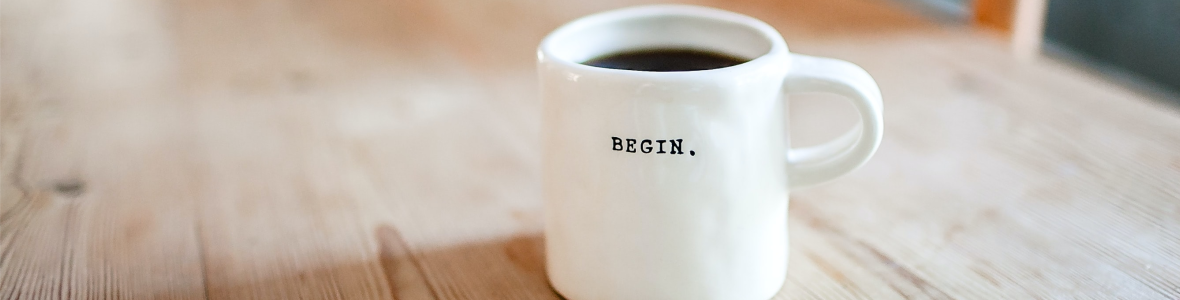 A white mug printed with the word BEGIN on a rustic wooden table